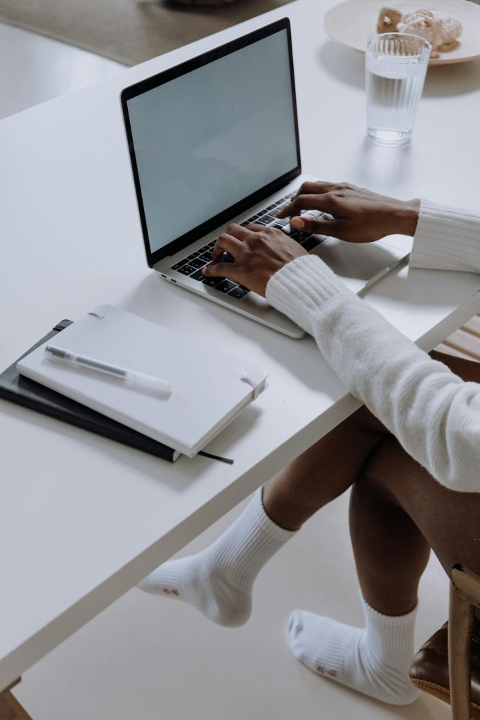 Someone sitting on their desk and typing on their computer. The scene is white and the college block besides it is empty