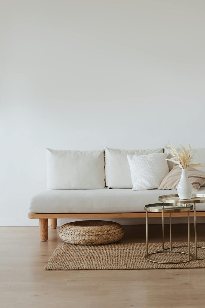 Minimalist living in form of a plain wall, a white couch, two side tables, very little decoration and a sitting pillow.