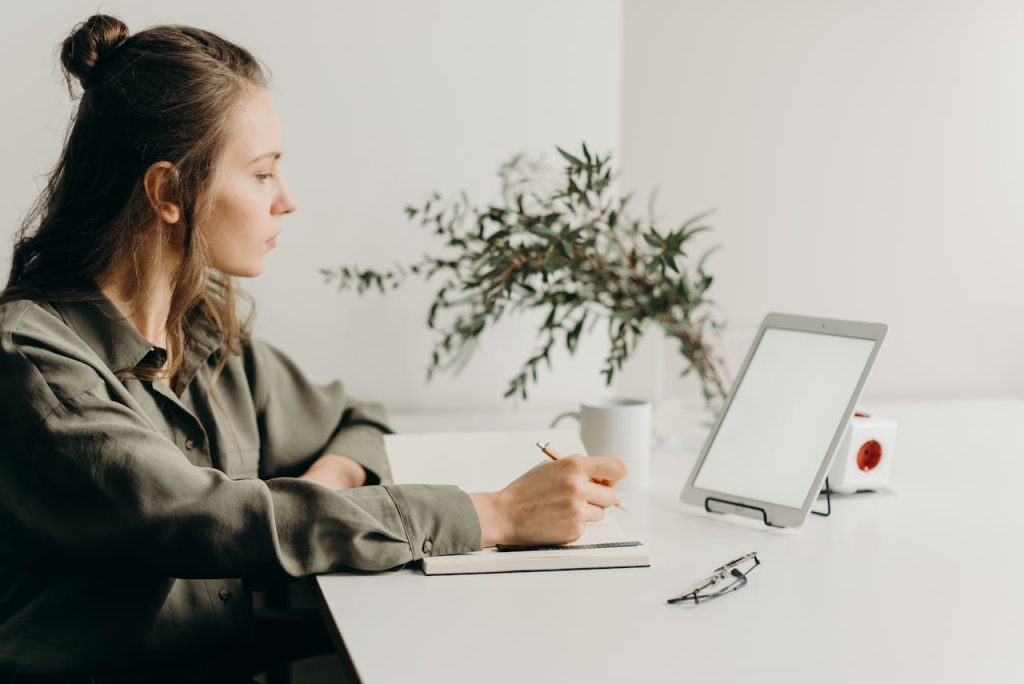 Woman looking very focused on a tablet while writing something down. The setup is very minimalistic.