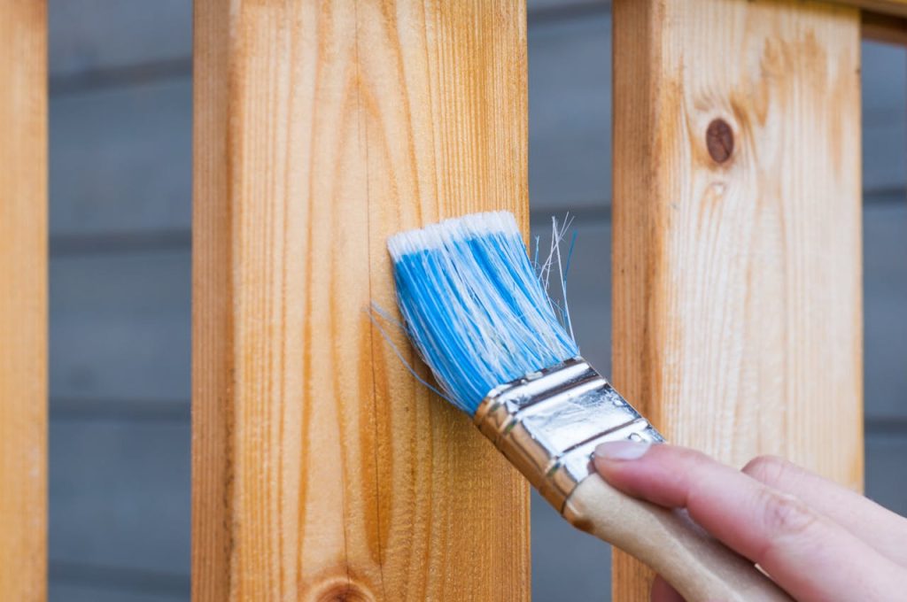 A hand is holding w paint brush painting a wooden fence