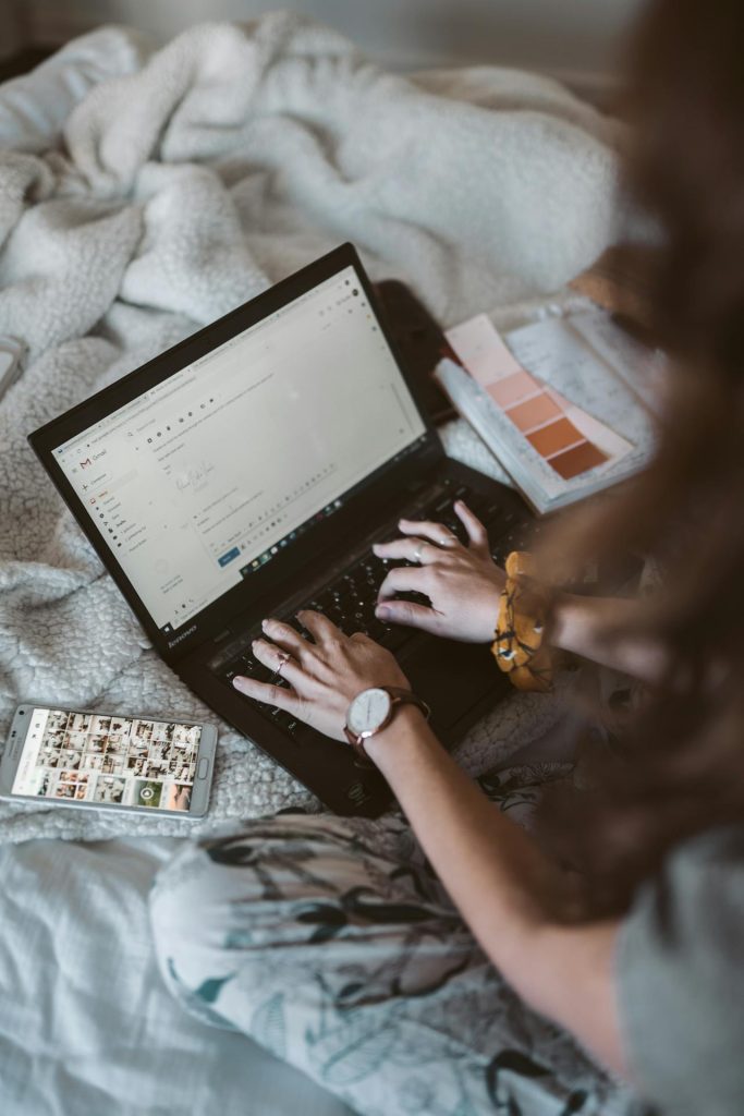 Someone working a computer with the phone lying next to it with photos being shown